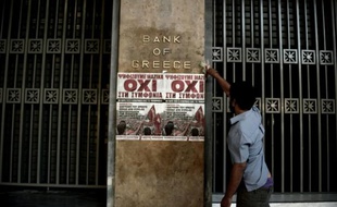 Un homme colle une affichette avec le slogan "No" sur la facade de la Banque de Grève, le 3 juillet 2015 à Athènes