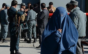 Une femme en burqa passe devant des policiers montant la garde devant le quartier général de la police à Kaboul, le 9 novembre 2014