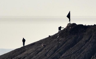 Des membres présumés du groupe Etat islamique près d'un drapeau du mouvement jihadiste, à proximité de la ville de Kobane, en Syrie, le 7 octobre 2014