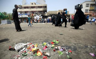 Des Irakiens passent à côté de fleurs et de chaussures laissées en hommage aux victimes d'un attentat à la voiture piégée, dans le quartier Sadr Area à Bagdad le 12 mai 2016