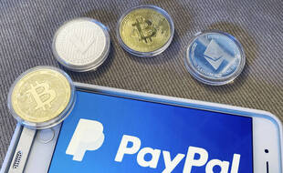 Le logo PayPal sur un smartphone et des pièces illustrant de la monnaie virtuelle.