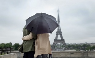 Un couple sous un parapluie observe la Tour Eiffel.