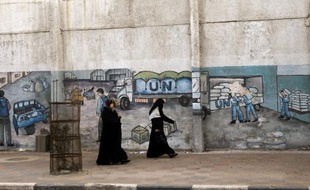 Palestinian women walk in front of graffiti next to the UN headquarters building in Gaza City on April 5, 2013. Gaza's Hamas rulers urged the United Nations to reconsider its suspension of food aid for Palestinian refugees, imposed after protesters stormed a UN depot. AFP PHOTO/MOHAMMED ABED
