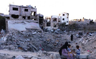 Photo du 11 aout 2014 montrant une femme et des enfants au bord du cratère où se trouvait autrefois sa maison démolie par une frappe israélienne à Jabalia dans le nord de la bande de Gaza