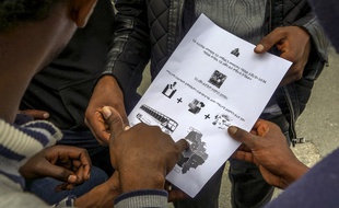 Des demandeurs d'asile lisent un document rédigé en langue Tigrinya pour leur indiquer le lieu de leur centre d'hébergement.