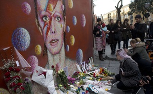 Des fans de David Bowie fleurissent un mur décoré d'un dessin en hommage au chanteur.