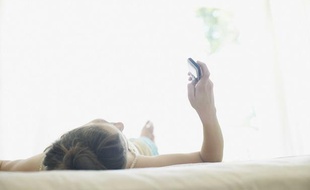 Femme sur un lit avec un téléphone.