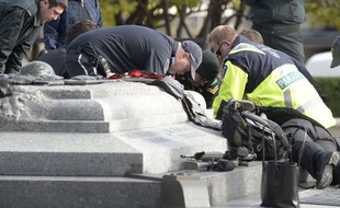Des ambulanciers portent les premiers secours au soldat blessé par balle devant un mémorial aux morts.