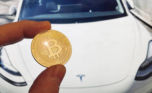 Une représentation d'un bitcoin devant une voiture Tesla.