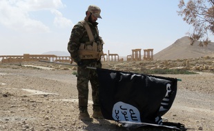 Un soldat de l'armée syrienne tient le drapeau de Daesh devant l'un des sites antiques de la ville de Palmyre, reprise dimanche 27 mars, par les troupes pro-gouvernementales. AFP PHOTO / STR