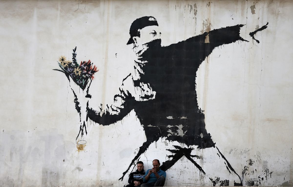 https://img.20mn.fr/U7hhSUkXTQuwQUHfNL0LVA/1200x768_two-men-are-sitting-in-front-of-a-famous-graffiti-of-british-street-artist-banksy-painted-on-a-wall