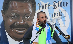 Omar Keddadouche devant la fresque en hommage à Pape Diouf lors de son inauguration.