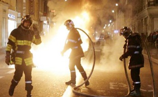Des pompiers éteignent une poubelle incendiée à Toulouse.