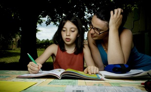 Une adulte aide un enfant à remplir son cahier de vacances.
