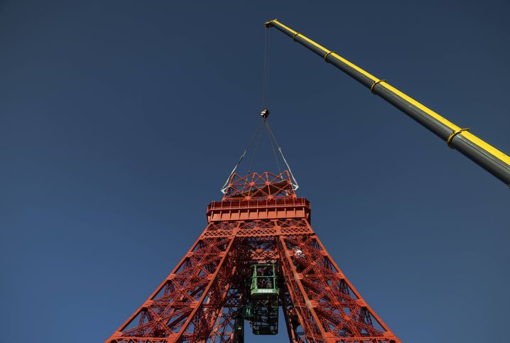 Une grue maintient la section centrale de la tour pendant que des ouvriers l’assemblent. 