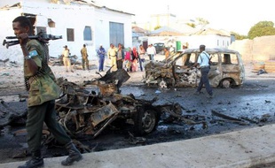 Un soldat somalien patrouille près de la carcasse d'un véhicule soufflé après un attentat-suicide à Mogadiscio, le 4 janvier 2014