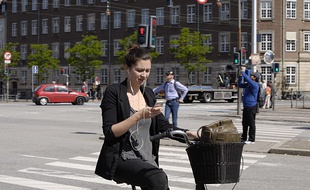 Une jeune femme regarde son téléphone alors qu'elle est sur son vélo (illustration).