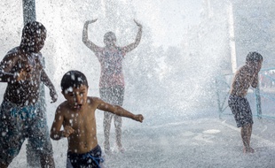 Des enfants et des adolescents jouent dans le jet d'eau d'une bouche incendie, à Aubervilliers le 30 juin 2015