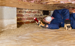 Termite inspector in residential crawl space inspects a sill for termites.