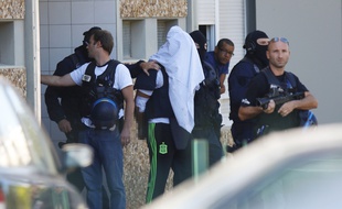 Yassin Salhi dont le visage est dissimulé, quitte son appartement entouré de policiers à Saint-Priest.