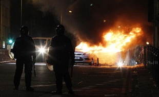 Des agents de police se teinnent près d'une voiture en feu, à Tottenham, au nord de Londres, le 7 août 2011.