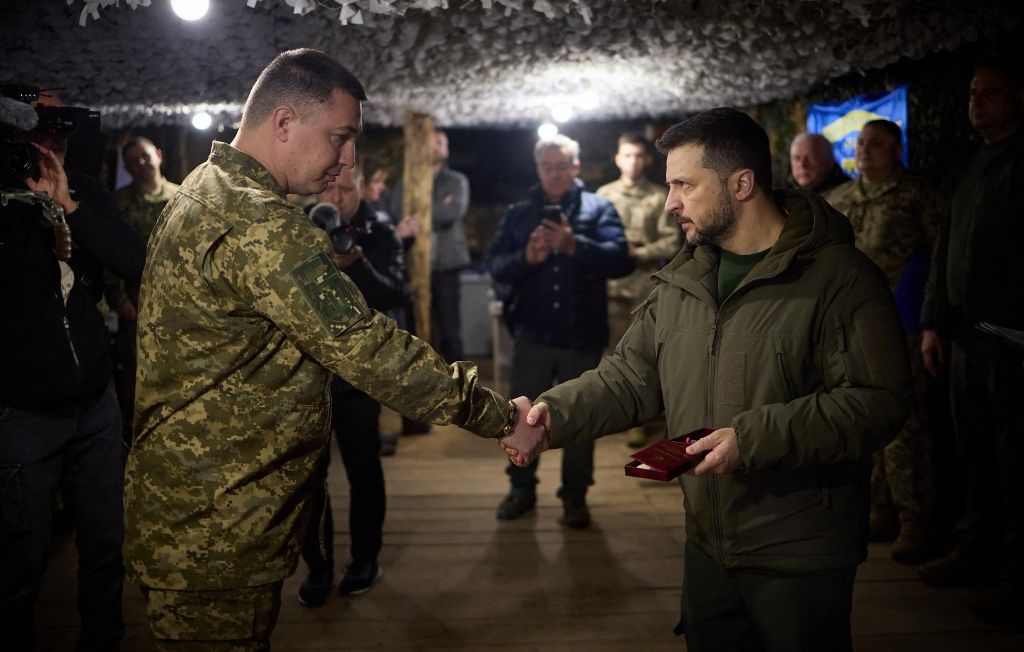 Le président Volodymyr Zelensky serre la main à des officiers sur l'une des lignes de défense ukrainienne dans la région de Sumy, le 27 mars 2024. 