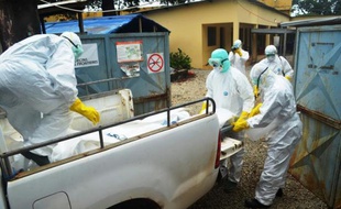 Des employés de la Croix-Rouge guinéenne, vêtus de combinaison de protection, transportent le corps d'une victime du virus Ebola, le 14 septembre 2014 à Conakry