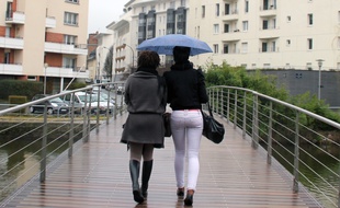 Deux jeunes femmes marchent sur un pont sous la pluie, ici à Rennes.
