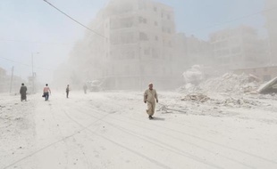 Des Syriens marchent dans le quartier Tariq al-Bab à Alep au milieu de la poussière après le largage d'une bombe-baril par l'armée le 7 juillet 2014