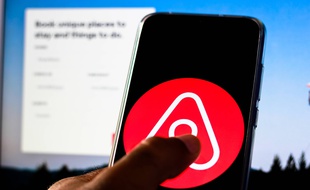 Un gros doigt devant le logo d'Airbnb. (illustration)