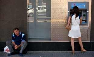 Un homme mendie pendant une femme retire de l'argent à Malaga le 27 juin 2014