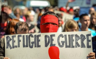 Un homme masqué tient une pancarte où est inscrit "Réfugié de guerre" lors d'une marche en mémoire des migrants morts en tentant de rejoindre l'Angleterre, le 8 août 2015 à Calais
