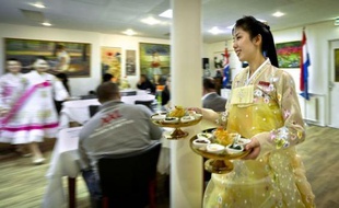 En robe cloche de soie jaune brodée, miss So accueille avec un sourire timide les clients du Pyongyang, le premier restaurant nord-coréen en Europe, selon ses propriétaires, qui vient d'ouvrir à Amsterdam.