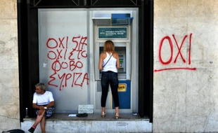 Une femme retire de l'argent à un distributeur bancaire non loin d'un mendiant et de graffitis disant "non à la peur", à Thessalonique, le 6 juillet 2015