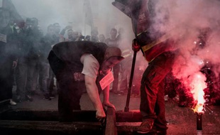 Un homme portant un masque représentant Emmanuel Macron et un autre gréviste de la SNCF déposent des rails devant le siège du Medef à Lyon le 1er juin 2016