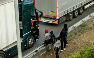 Des migrants parlent avec un camionneur se dirigeant vers l'Eurotunnel à Coquelles, près de Calais, le 29 juillet 2015
