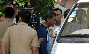 Un réfugié pris en charge par l'Australie dans l'île de Nauru, dans le Pacifique, est conduit sous escorte policière jusqu'à un véhicule à son arrivée le 4 juin 2015 à l'aéroport de Phnom Penh, la capitale du Cambodge
