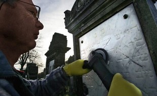 Un homme tente d'effacer des inscriptions nazis sur une tombe, illustration