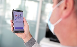 Un homme masqué regarde son téléphone, et là, oui, l'application TousAntiCovid apparaît.