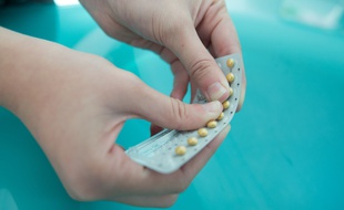 Une jeune femme adolescente en train de prendre une pilule contraceptive dans sa salle de bains. (Illustration)