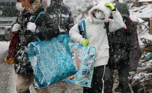 Des survivants repartent vers leur refuge après avoir récupéré quelques affaires parmi les décombres de leurs maisons à Natori dans la préfecture de Miyagi, le 17 mars 2011.