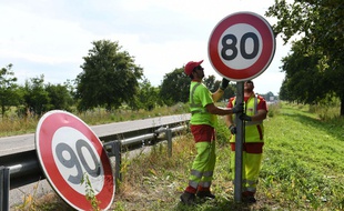 Des hommes changent le panneau de vitesse sur une route départementale.