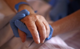 Illustration: Une infirmière portant des gants de protection tient la main d'un patient en unité de soins palliatifs à l'hôpital Eugénie d'Ajaccio, le 23 avril 2020.