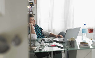 Un homme qui travaille chez lui avec un téléphone et un ordinateur.