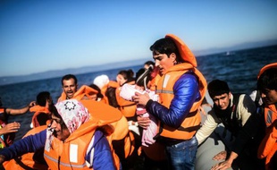 Une homme porte un nouveau né à son arrivée avec d'autres réfugiés sur l'île de Lesbos en Grèce, après une traversée en canot pneumatique de la mer Egée depuis les côtes turques, le 12 novembre 2015