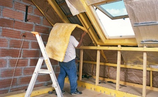 Un artisan dépose un rouleau de laine de verre entre les éléments structurels de la toiture pour l'isoler thermiquement les combles.