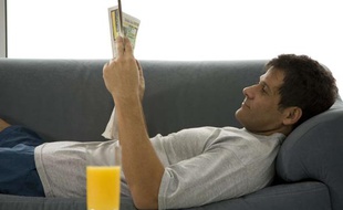 Un homme lit le journal sur son canapé.