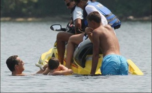 Sur des clichés pris par un photographe de l'AFP depuis le lac à Springfield Point, on peut voir le chef de l'Etat français, nageant avec ses lunettes de soleil, s'approcher en souriant d'un jet-ski jaune sur lequel se trouvent deux adultes et un adolescent.