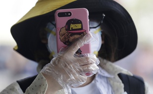 Une femme utilise des gants pour tenir son smartphone le 18 mars 2020 à Manille aux Philippines.