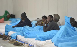 Des migrants se préparent à passer la nuit dans un hangar aménagé et chauffé dans le cadre du déclenchement du niveau 2 du plan grand froid, le 27 décembre 2014 à Calais
